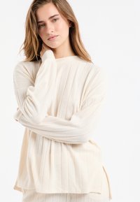 Hellbeiger gerippter Pullover mit langen Ärmeln und rundem Ausschnitt. Verfügt über seitliche Schlitze und einen weichen, strukturierten Stoff.