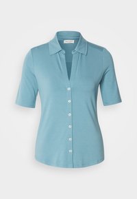 Chemise à manches courtes bleu clair avec un col, un boutonnage sur le devant et une texture douce. Comprend six boutons blancs le long de la patte de boutonnage.