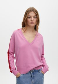 Rosa gestrickter Pullover mit V-Ausschnitt, kontrastierenden roten Streifen an den Ärmeln, gerippten Bündchen und Saum. Glatte Textur mit einem schlichten Design.