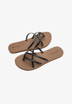 Des tongs à brides noires avec une semelle en caoutchouc beige, présentant deux brides croisées et le logo "VOLCOM" en relief sur la semelle intérieure.