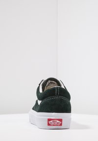 Grüne Wildledersneaker mit weißen Akzenten, flacher weißer Sohle und rotem Logostreifen an der Ferse. Mit gestickten Details und runder Zehenform.