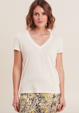 Crème V-hals t-shirt gemaakt van zachte stof, met korte mouwen en een delicate afwerking bij de halslijn, gecombineerd met een gemusterde rok.