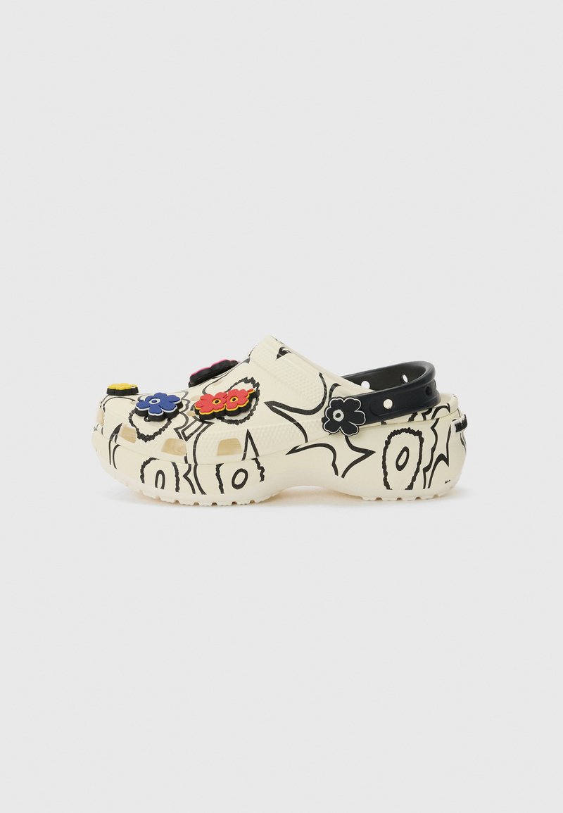 Crocs clogs in cream with black floral doodle art. Features black heel strap, ventilation holes, and colorful flower charms attached.