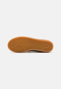 Brown rubber outsole with a herringbone pattern, featuring a smooth edge for grip and stability. The center has a slight curve for flexibility.