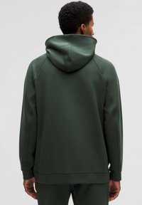 Vihreä huppari rentoa istuvuutta, jossa on suuri huppu, sileä tekstuuri ja raglanhihat. Yksinkertainen muotoilu ilman näkyviä logoja tai kuvioita.