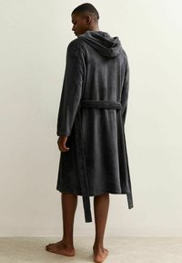 Grijze fleec bathrobe met een capuchon, strikomslag, en lange mouwen, met een zachte textuur en een middellange snit. Draagt door een persoon die zijwaarts staat.