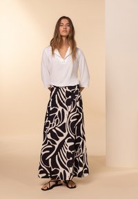 Blusa bianca a colletto, gonna maxi nera e crema con motivi a foglia, e sandali neri. Tessuto liscio e vestibilità ampia.