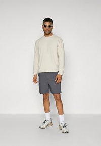 Šviesiai pilkas džemperis su apvalia iškirpte, tamsiai pilkos šortai, baltos kojinės ir šviesūs sportbačiai. Akiniai nuo saulės užbaigia laisvalaikio aprangą.