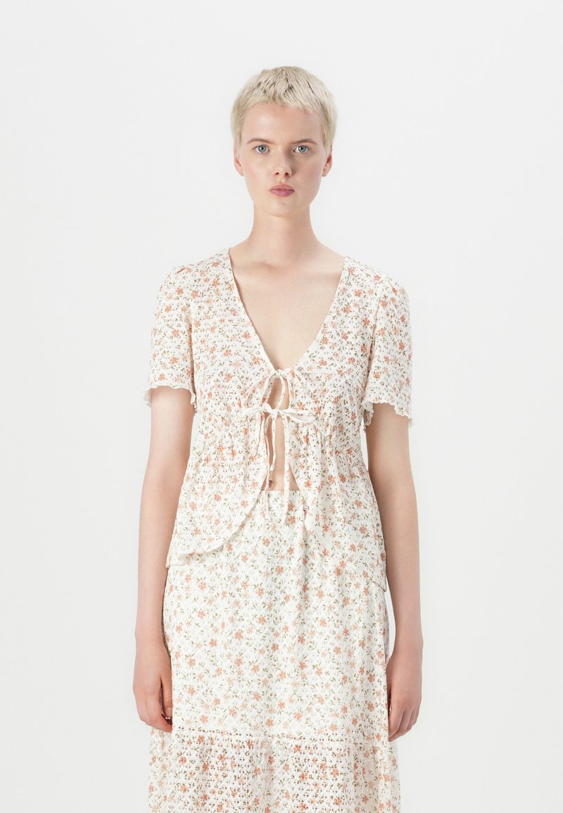 Robe blanche à manches courtes, ornée d'un motif floral dans des couleurs pastel, avec un décolleté en V profond et un lien à la taille.