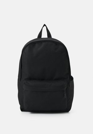 Sac à dos noir avec une poche zippée à l'avant, un compartiment principal zippé et une boucle de portage supérieure sur un fond clair uni.
