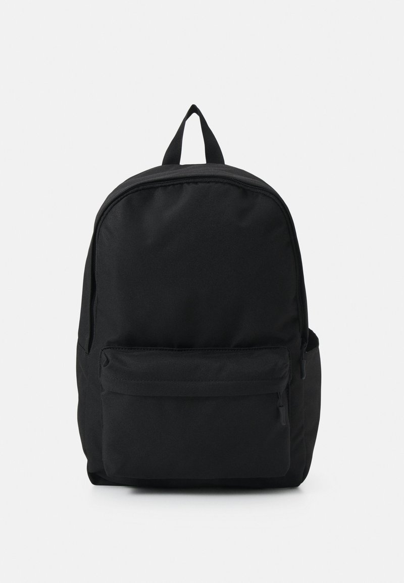 Sac à dos noir avec une poche zippée à l'avant, un compartiment principal zippé et une boucle de portage supérieure sur un fond clair uni.