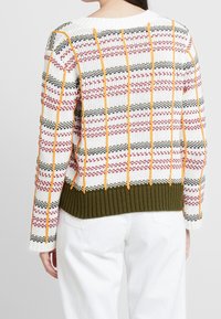 Suéter de punto en blanco con patrones de rayas en rojo, negro y naranja; dobladillo acanalado en verde oliva; corte relajado; mangas largas.