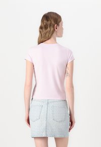 Világos rózsaszín, rövid ujjú felső, cropped fazon. Farmer szoknyával viselve, amely ismétlődő mintával és két hátsó zsebbel rendelkezik.