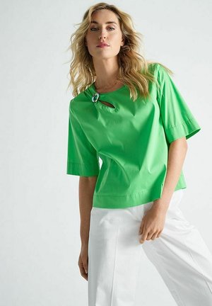 Groen blouse met korte mouwen en een ronde halslijn, voorzien van een decoratief accent bij de kraag, gecombineerd met witte wijde broekspijpen.