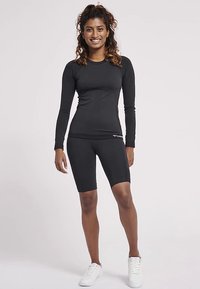 Svart långärmad topp och shorts av stretchigt material. Enkel design med tajt passform och minimal märkning vid fållen. Vita sneakers.