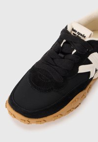 Black sneaker featuring a suede upper with white accents, round laces, and a textured gum rubber outsole. Logo visible on the tongue.