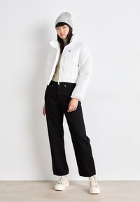 Vit kort puffjacka med dragkedja, svarta jeans och krämfärgade sneakers. Grå stickad mössa ger värme till outfiten.