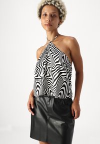 Halter top s čierno-bielym vlnitým vzorom vyrobený z hladkej tkaniny, v kombinácii s priliehavou čiernou koženou sukňou s postranným švom.