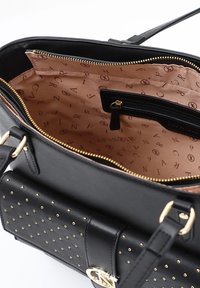 Borsa nera con un'esterno testurizzato caratterizzato da borchie dorate, una parte superiore con zip e un rivestimento beige stampato con logo. Include una tasca interna.
