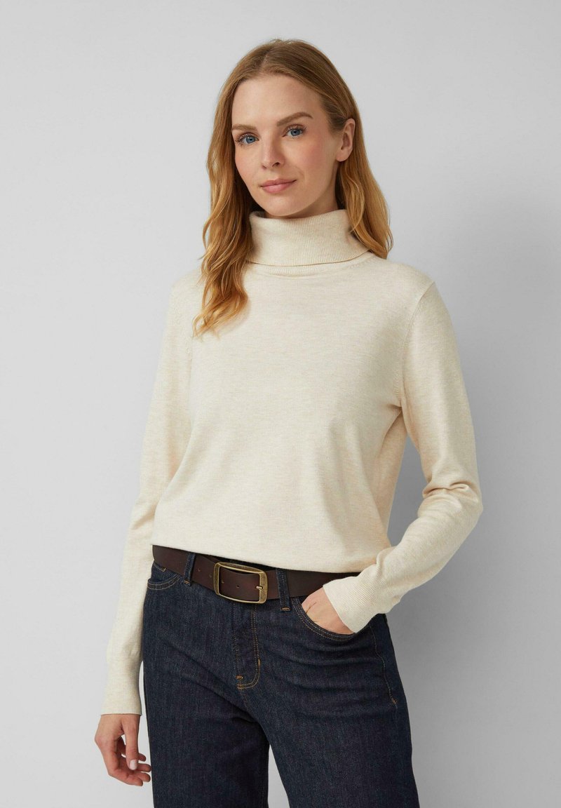 Beige coltrui van zacht materiaal, met lange mouwen, een relaxte pasvorm en een geribbelde kraag, gecombineerd met donker denim jeans en een brown riem.