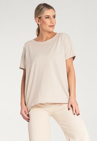 Beżowa bluzka z krótkim rękawem, wykonana z gładkiego materiału, o luźnym kroju i okrągłym dekolcie. Posiada subtelny akcent po bokach przy dolnej krawędzi.