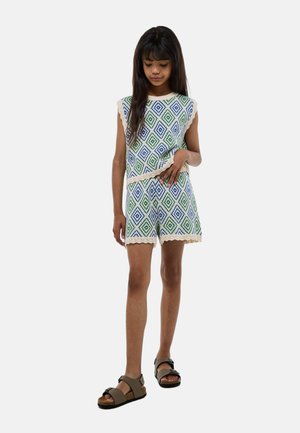 Combi-short à manches courtes en blanc avec des motifs en diamants bleus et verts, des bords festonnés et des accents beiges. Associé à des sandales marron.