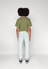 Camiseta verde de manga corta combinada con jeans rectos de tiro claro. Presenta una etiqueta de marca visible en los jeans y zapatillas negras.