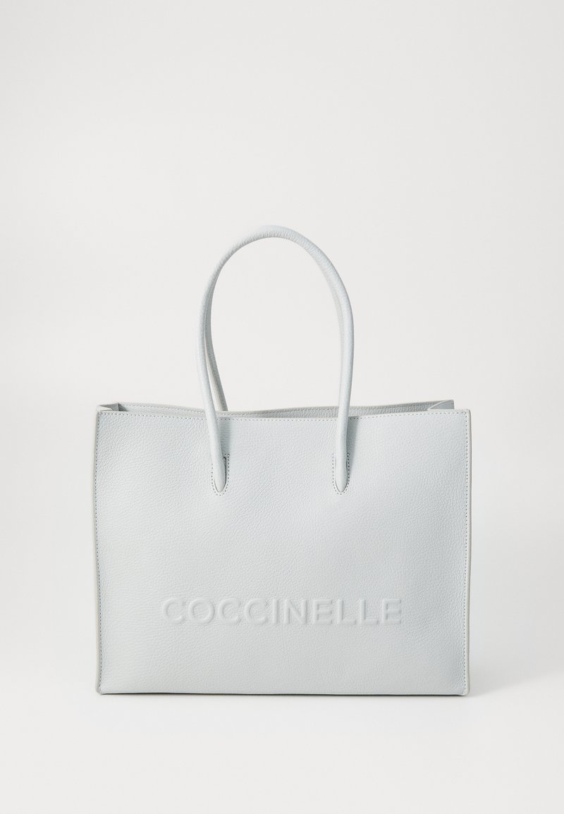 Svijetlosiva kožna torba s otisnutim logotipom "COCCINELLE". Ima dva čvrsta ručka i strukturiran oblik. Minimalistički dizajn.