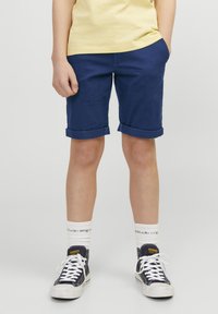 Navy blå bomullsshorts med rullet kant, kombinert med hvite sokker og svarte joggesko. T-skjorten er lysegul.