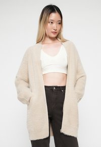 Beige, oversized cardigan gemaakt van een zachte, gestructureerde stof. Het heeft een brede kraag, een open voorkant en zijzakken.