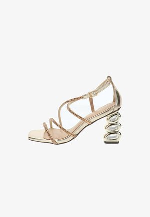 Sandalia dorada de mujer con tiras finas adornadas y un tacón metálico escultórico en bloque, con cierre de hebilla en el tobillo.