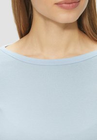 Haut bleu clair à manches courtes avec un col bateau, fabriqué à partir d'un tissu doux et lisse, présentant une texture subtile et des bords nets.