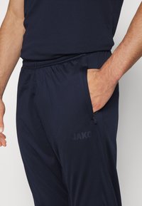 Marineblaue Sporthosen aus leichtem Stoff, mit einem elastischen Bund, seitlichen Taschen und einem dezenten Logo in passender Farbe.