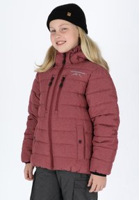 Giacca a vento bordeaux con chiusura zip, due tasche sul petto e polsini elasticizzati. Indossata con un berretto di maglia nero, che mette in evidenza la texture trapuntata.