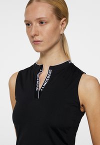 Black sleeveless polo shirt with a zippered collar, featuring a white logo trim. Made from a smooth fabric with a fitted design.
