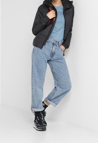 Sort pufferjakke med hætte, lyseblåt top, lyseblå baggy jeans og sorte sportssko med hvide accenter. Afslappet outfit.