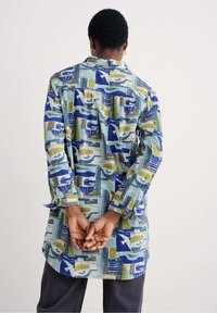 Patterned long shirt featuring geometric designs in blue, green, and yellow, made from a lightweight fabric, with a loose fit and long sleeves.