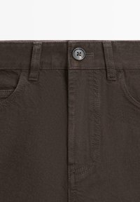 Donkerbruine denimbroek vooraan met knoopsluiting, broekriemlussen en stiksels van de voorzakken.