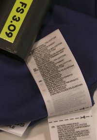 Mornarski uzorak tkanine s teksturiranom površinom i etiketa za njegu koja prikazuje sastav materijala, uključujući postotke pamuka i poliestra.