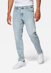 Jeans de mezclilla de lavado claro con un diseño de pierna recta, un leve desgaste, cinco bolsillos y un cierre de botón. Combinados con zapatillas blancas.