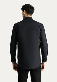 Camisa negra de manga larga con cuello clásico, textura suave y puños abotonados; presenta un diseño de espalda recta sin patrones.