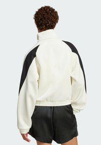 White and black color-blocked jacket with a high collar, oversized sleeves, and elastic cuffs, paired with black satin shorts.