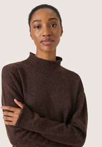 Brauner Pullover mit hohem Kragen, langen Ärmeln und einer weichen, strukturierten Optik. Hat eine lockere Passform und minimale Nähedetails.