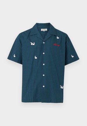 Kurzärmeliges kariertes Hemd in Dunkelblau mit weißer Kaninchenstickerei; abgenutzte blaue Jeans mit herzförmigen Ausschnitten; schwarze Schuhe.