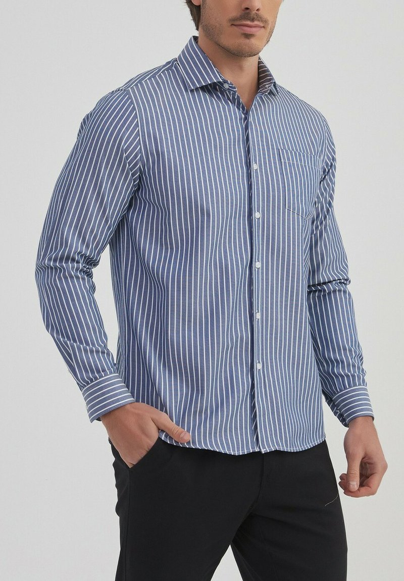 Chemise pour homme à boutons en coton, avec des rayures verticales bleues et blanches, des manches longues, un col et une poche sur la poitrine.