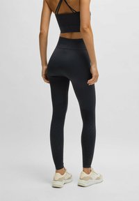 Mustat legginsit, joissa on korkea vyötärö, virtaviivainen istuvuus, teksturoitu kuvio ja ne on paritettu vaaleiden lenkkareiden kanssa. Pehmeä kangas, jossa on sileä pinta.