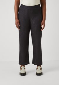 Black textured wide-leg pants with a patterned fabric, featuring a stretchy waistband. Worn with light-colored slip-on shoes.