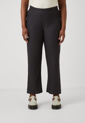 Black textured wide-leg pants with a patterned fabric, featuring a stretchy waistband. Worn with light-colored slip-on shoes.