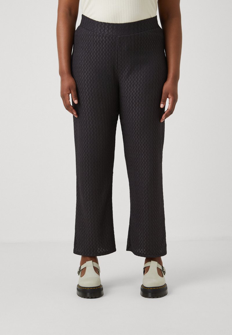 Black textured wide-leg pants with a patterned fabric, featuring a stretchy waistband. Worn with light-colored slip-on shoes.