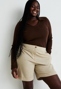 Top marrón de manga larga y pantalones cortos beige hasta la rodilla con cierre de botón. Textura suave, diseño sencillo y corte recto.
